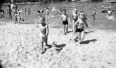 Grybe golf, Gustavsvik 17 juni 1967

Fem pojkar i sexårsåldern har precis klivit upp ur utomhusbassängen i Gustavsvik. Pojken till vänster har vita badbyxor och de andra tre har mörka badbyxor. En kvinna i baddräkt och en liten flicka i bikini med en liten blus över och en hink i vänstra handen kommer upp ur vattnet till vänster.