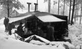 Manöver i Kilsbergen 1 21 februari 1967

Fyra militärer står inne i ett öppet militärtält i Kilsbergen. De är i färd med att äta. En byggnad syns i bakgrunden. Det ligger fullt med snö på marken.
