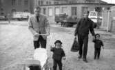Med pappa på turné 14 april 1967

Den kände skådespelaren Helge Skoog går tillsammans med sina ettårsgamla barn och en annan man utanför Norlings bryggeri. Helge kör en vit barnvagn med dubbelsits. Det ena barnet håller i barnvagnen och den andra håller den andra mannen i handen. Helge är klädd i vit kavaj, beige skjorta, svart slips och svarta byxor. Barnen är klädda i svarta dressar med små hattar på huvudena. Den andre mannen är klädd i svart jacka svarta byxor, randig skjorta och svarta skor. Han bär en rutig väska i ena handen.
