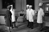 Minnesutställning se, Sockerbagare hos Thyra 7 april 1967

Fyra sockerbagare i vita arbetskläder med vita hattar till står inne i ett stort rum och samtalar med äldre dam i svart dräkt och med vita pärlor runt halsen. I bakgrunden syns fåtöljer samt stora tavlor som hänger på väggarna.