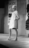 Modevisning, Görtz motor (Rep av oil) 6 april 1967

Under en modevisning poserar en fotomodell på scenen. Hon är klädd i en vit kappa, vit hatt och har silverskor på fötterna. En skylt med delvis dold text hänger på väggen bakom henne.