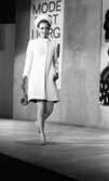 Modevisning, Görtz motor (Rep av oil) 6 april 1967

En fotomodell går på scenen under en modevisning. Hon är klädd i en vit kappa, vit hatt, örhängen, pumps på fötterna, handskar och hon håller en handväska i höger hand. Bakom henne på väggen hänger en skylt med texten: 