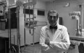 Lungkliniken, Nappivalen, Grekiskt handarbete 11 december 1967

En läkare i vit läkarrock, vit skjorta, svart fluga, mörkgrå byxor och svarta skor. En stor röntgenapparat står bakom honom (medicinsk utrustning). Flera fönster syns i bakgrunden även.