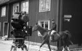 Wadköping 2 TV-inspelning, 31 maj 1968

Under TV-inspelningen av Markurells i Wadköping rider en man som är skådespelare genom Wadköping på en häst. Han är klädd i 1800-talskläder. En stor filmkamera står i förgrunden på ett stativ.