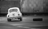 Wv Bilnytt 24 november 1967

En man testkör en vit folkvagn på en asfaltplan. Bildäck ligger utplacerade på marken och han kör bilen i sicksack mellan dem. Byggnader syns i bakgrunden.