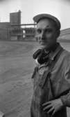 Ytong 30 november 1967

Närbild på en man som arbetar på Ytong. Han är klädd i mörka snickarbyxor med en ljus skjorta under samt en ljus keps på huvudet. Han har hörselskydd som han har hängt runt sin hals för tillfället. En industribyggnad syns i bakgrunden.