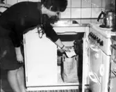 Kvinlig hyresgäst visar det moderna kökets sophantering i Rostaområdet på 1950-talet.