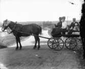 Häst med vagn, fyra personer i vagnen.