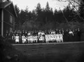 Grupp, bröllop, brudpar och bröllopsgäster.
Bostadshus till vänster på bilden.