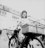 Konsums springflickor, en flicka med cykel.
Affärsbyggnad i bakgrunden.