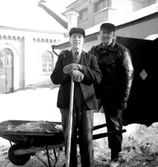 Fo-staben, två män med skottkärra.
Byggnader i bakgrunden.
Till höger Harald Falk, medlem i Ornitologiska Klubben Örebro.