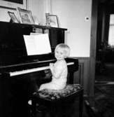 Rumsinteriör, en pojke vid pianot.
Fru Larsson