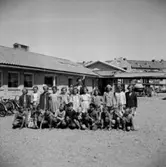 Hagaskolan, skolbarn med lärare på skolgården.
Skolbyggnad i bakgrunden.
Fröken Olsson