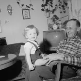 Rumsinteriör, en man och ett litet barn.Fru Britta Jönsson (beställare ?).