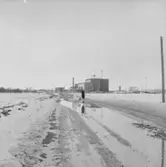 En kvinna med ett barn i barnvagnen.
Patrik och Plutt.
Byggnad i bakgrunden.