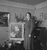 Rumsinteriör, en kvinna, högtid.
Fru Falk