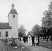 Brudpar och bröllopsgäster, kyrkobyggnad i bakgrunden.
Ragges bröllop i Stora Mellösa kyrka.