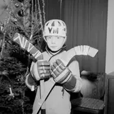 Rumsinteriör, en pojke i ishockeydräkt vid julgranen.
Hasse