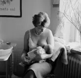 Rumsinteriör, en kvinna och en baby, amning.
Plutt och Patrik.