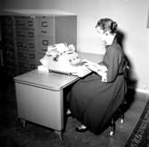 Kontorsinteriör, en kvinna vid skrivbordet.
Wigrell & Co, utställning på Idrottshuset.