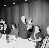 Rumsinteriör, grupp vid bordet. Personalklubben uppvaktar, Majgren avtackas.
Örebro Kexfabrik.