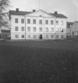 Byggnader. 
27 november 1942.
Huset var fram till 1929 Nora stads enda skolhus. 1929 byggdes färdig en ny skola vid Skolgatan. På 1950-60-talet var det rådhus.
Lilla huset bakom till vänster är Thela Bloms hattaffär. Till höger på bilden Konsum affär.