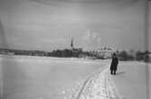 Vintermotiv. En man vid Lindesjön.
Kyrkobyggnad och bostadshus i bakgrunden.