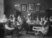 Dövstumskolan, klassrumsinteriör, syslöjden, 17 skolflickor med lärare.
Till folkskoleboken.