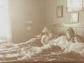 Interiör från sängkammaren, tre personer i sängen.
Gerda Thermaenius med döttrarna Maj och Barbro.