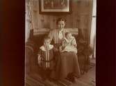 Rumsinteriör, en kvinna med två barn.
Anna Gustavsson (Gavenius) född Thermanius, med barnen Bertil och Lisa.
