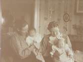 Rumsinteriör, två kvinnor och två småbarn.
Från vänster Anna Gustavsson med dottern Anna-Greta och Edith Nerell med dottern Ingrid.
Anna och Edith var döttrar till Edvard och Jenny Thermaenius. Bilden tagen i 