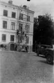Bostadshus i fyra våningar. Arbetare på byggnadsställning.
Två bilar framför byggnaden.
Bilden tagen i slutet av 1930-talet.