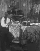 Rumsinteriör, en yngre man vid ett kaffebord. Troligen tagen 1915-1920. Lars (givaren) känner inte igen mannen men säger att den ju kan vara tagen på pensionaten liksom den förra bilden nr. 9.