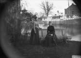 Två kvinnor.
Hamnmagasinet och en ångbåt i bakgrunden.
Bilden är tagen på 1880-talet. Båten 