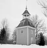 Bystad (Bysta) den 23 mars 1937. Den fristående klockstapeln, som hör till kyrkan, är gjord av trä och målad i gul färg (framgår ej av bilden). På det nedre takets alla fyra sidor finns varsin klocka med urtavla. Över det nedre taket finns själva kyrkklockan i ett utrymme med fria öppningar ut, och längst upp ett övre tak med en liten lökkupol och en vindflöjel. På vindflöjeln står det 