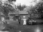 Två män och en kvinna samt fem barn står i trädgården framför huset 