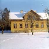 Bystad skola.
Skolhuset, fasaden mot trädgården, på vinter.
Bilden har i kanten en tryckt text: 