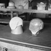 Lindbergs Strå- och Filth. Hattillverkning. 213/67 Mössform för hatt utan brätten, av trä med tryckstycke av aluminium. Den färdiga hatten till vänster sitter på ett hattstöd av papp.