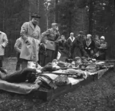 Samrealelever vid skjutbanan.
Stående i rock och hatt magister L. Ranch.
Miltärklädd, Gunnar Granberg.
Skolfröken som antecknar, Kerstin Rickardsson.