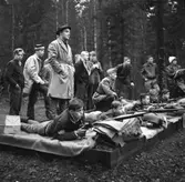 Samrealelever vid skjutbanan.
Stående i rock och hatt magister L. Ranch.
Miltärklädd, Gunnar Granberg.
Skolfröken som antecknar, Kerstin Rickardsson.