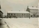 Stora torget. Omkring 1912. Den s.k. Thulins-tomten vid Stora torget. Utanför sin butiksdörr står gamle glasmästare  A. Larsson, därnäst (åt höger) är Kristinedals fabriksbod, och ännu längre till höger synes Hilma Brelins vita skylt. Ingången till hennes affär var från gårdssidan. I gatuhörnet står fastighetens ägare byggmästare Emil Gustafson (fr.Motala).