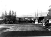 Byggnadsarbete pågår med viadukten. Vägport och väganläggning avsynad 8 febr. 1939. Den nya utfartsleden delar sig vid Danska Vägen med en väg åt Göteborg och en del norrut. Mössebergs långsträckta kontur i bakgrunden.