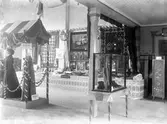 Interiör från Östra härads lantbruks- och industriutställning 1907. Till vänster syns kläder från Karl Sjöstrand.