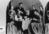 Grupp nio personer vid kaffebordet, i Wilhelmina Lagerholms fotoateljé (1863-1866), Drottninggatan 43, Örebro.
Personerna på bilden är: 
- Augusta Toll, född Kalling, död 1906.
- Louise Gripenberg
- Löjtnant V. Falkman
- Agneta Årman (i Mellösadräkt)
- Anna Elisabeth Lagerholm (född Ekman), Wilhelmina Lagerholms mor.
- Wilhelmina Lagerholm (1826-1917)
- Sophia Gripenberg
- Anna Lundberg, född Kalling, död 1930.
- Maria Gripenberg