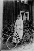 En kvinna med cykel.
Bostadshus i bakgrunden.
Alma Holmberg