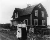 Tvåvånings bostadshus, tre personer framför huset.
Bertil Lindby med mor och mormor.