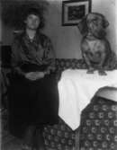 Rumsinteriör, en flicka och en hund på bordet.
Thora Engstedt, fosterdotter hos L.J. Juhlin och hunden Lassi.
