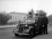 Två poliser utanför sin polisbil  (högtalarbil) av
märket Volvo, parkerad vid Fabriksgatan 1 i Örebro.
 Polisen till höger är John Fallin.
I fonden Vasabron och Nämndhuset.
Bilden tagen på 1930-talet.