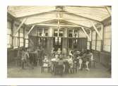 Leksalen i gamla paviljongen på Kustsanatoriet Apelviken. Grupper av barn sitter kring bord, en pojke sitter på en hjulförsedd trähäst till höger.