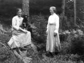 Gruppbild av två kvinnor och en hund fotograferade utomhus i en skog.
